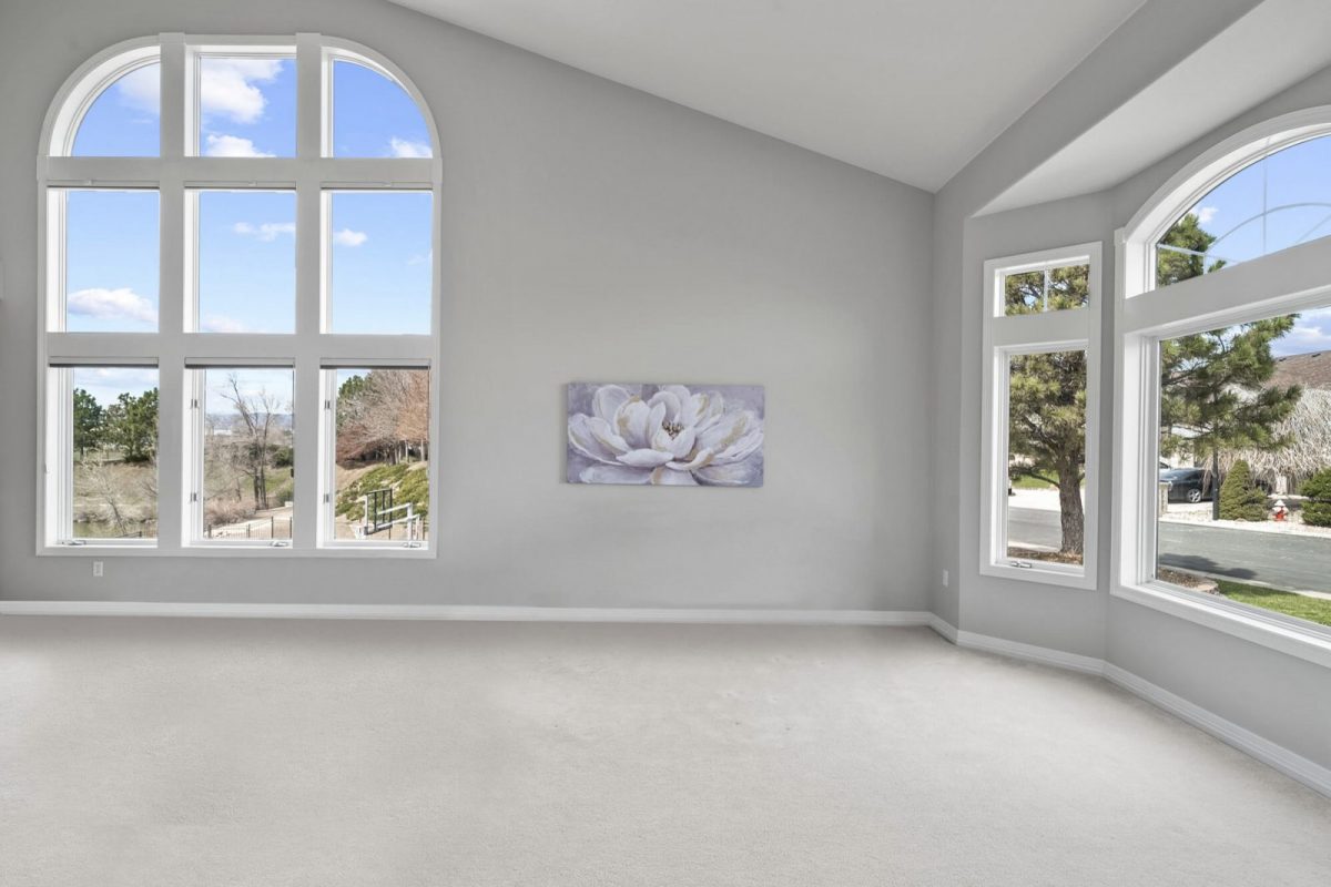 The same living room empty, with tall arched windows and pale carpet