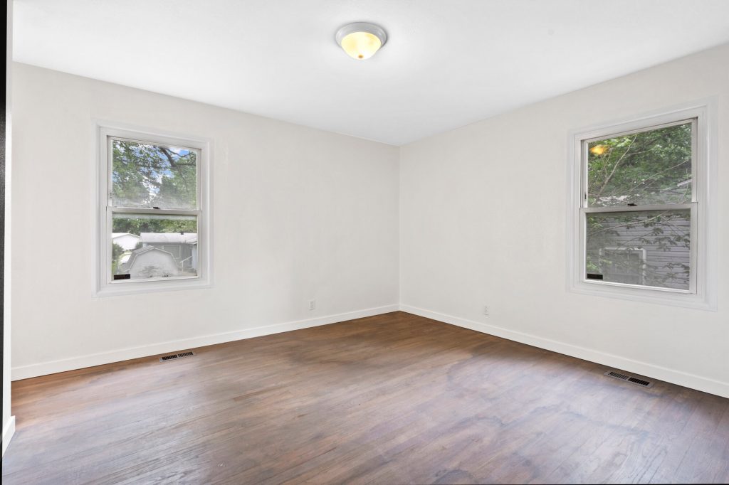 Empty bedroom with wood floors and two windows, before virtual staging