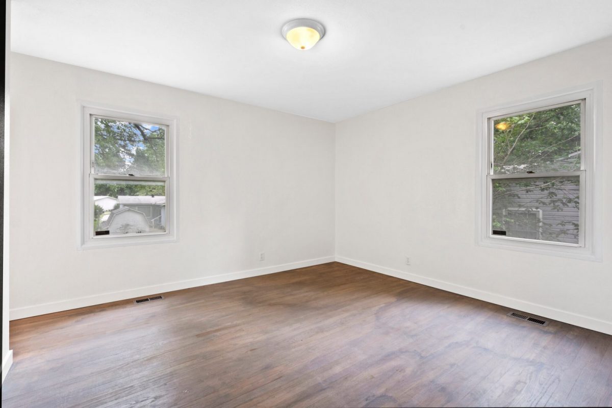Empty bedroom with wood floors and two windows, before virtual staging