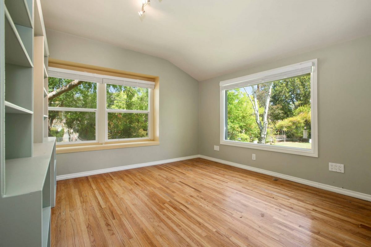 Empty room with wood floors, built-in shelves and two large windows