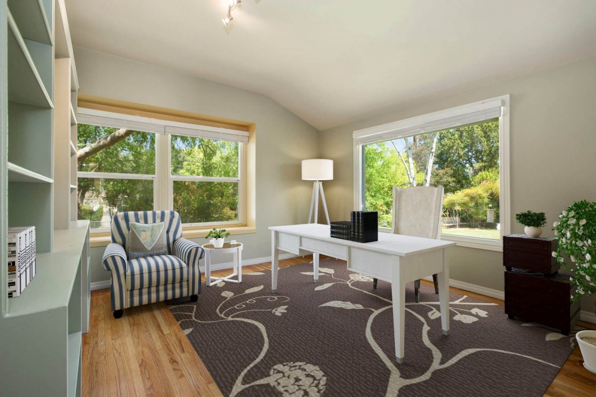 The same room virtually staged as a home office with a desk, armchair, rug and shelving